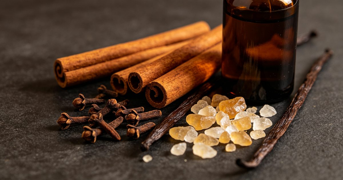 Cinnamon bark, cloves and vanilla pods with resin pieces beside a dark bottle