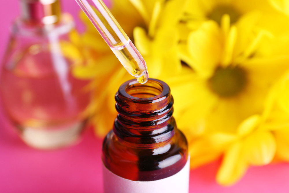 Amber glass dropper bottle with a drop of fragrance oil being dispensed, set against yellow flowers